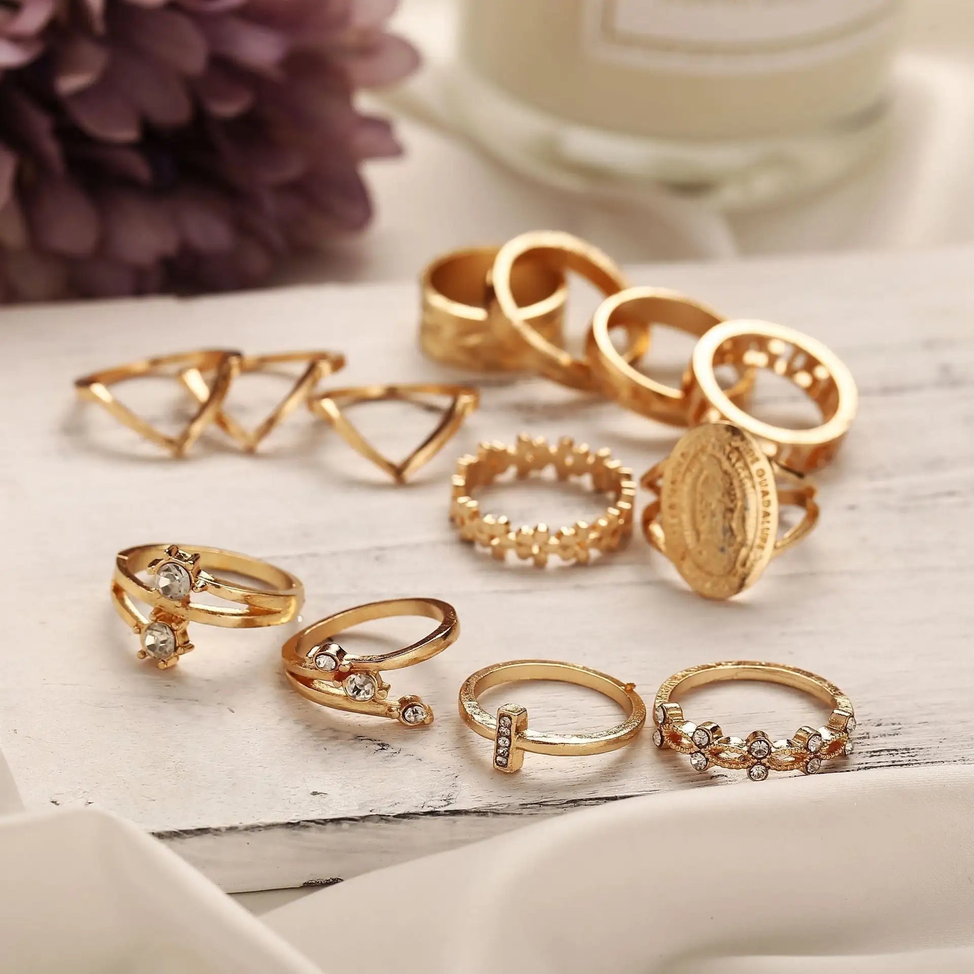 Collection of 13 gold rings featuring Austrian crystals in various styles on a wooden surface.