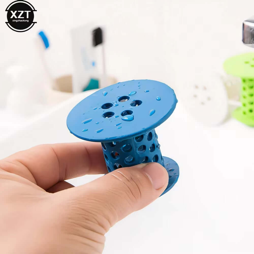 Hand holding a blue versatile bathroom drain hair catcher and stopper over a sink with droplets on it.