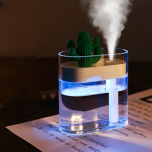 LED ultrasonic air humidifier with cactus design, emitting mist, set on a light-colored surface.
