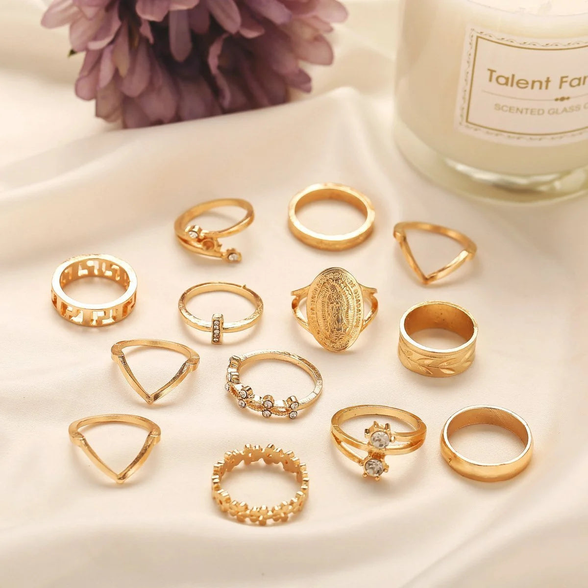 13-piece set of gold-tone rings featuring Austrian crystals, displayed on soft fabric with a scented candle.