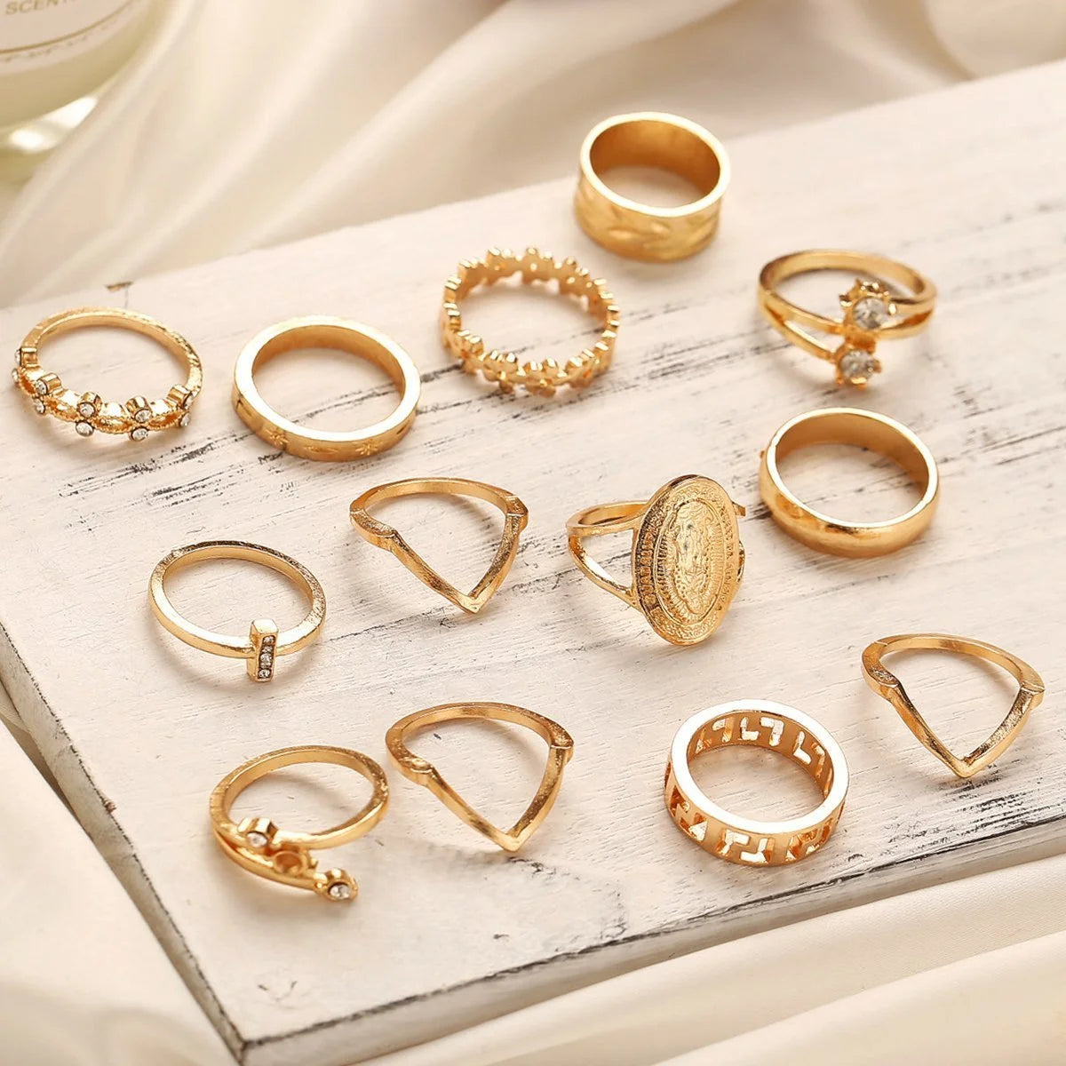 13-piece gold ring set featuring various styles, including medallions and geometric designs on a wooden surface.